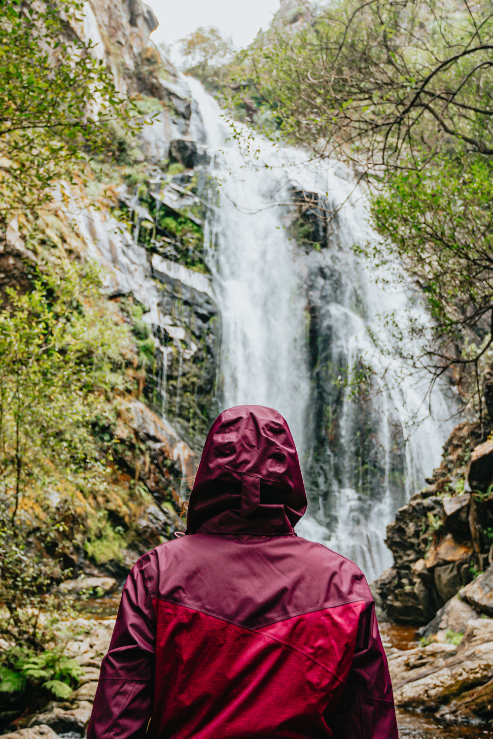 person-in-red-raincoat-admires-a-huge-waterfall